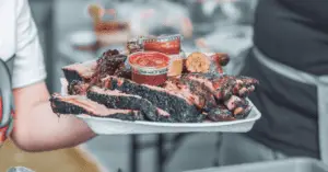A White Plate Being Carried Full of Pinkish and Charred BBQ that Appears to have just recently come off the grill. 